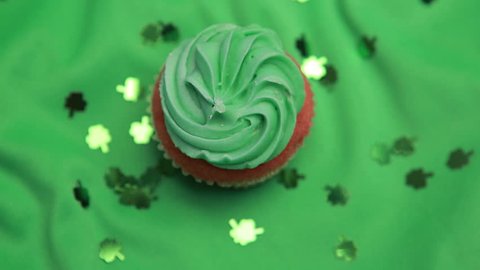 St patricks day cupcake revolving with shamrock confetti falling on green surface Stock Video