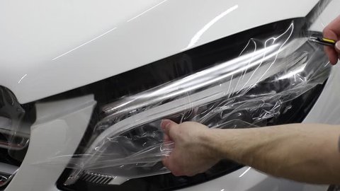 Close up shot of the hands of man who unstick the film with white cowl expensive car. This film protects the vehicle from the rough painting. car wrap protection film paint
