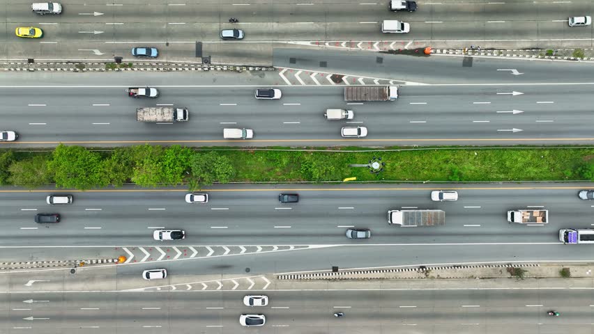 From above, witness a bustling multi-lane thoroughfare with cars, a motorbike, and a towering truck, each confined within crisp lane dividers, epitomizing the dynamic pulse of transportation.
 Royalty-Free Stock Footage #3502417989