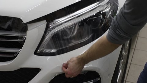 Close up shot of the hands of man who unstick the film with white cowl expensive car. This film protects the vehicle from the rough painting.