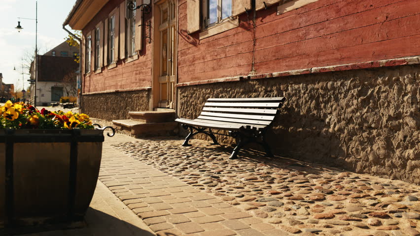 Bench outside red building on sidewalk with plants
