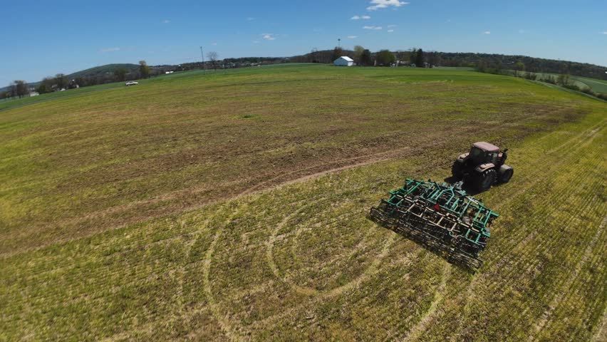 Tractor pulling plowing machine on farm field in America during sunny day. Spring season preparation of field. Aerial fpv tracking shot.