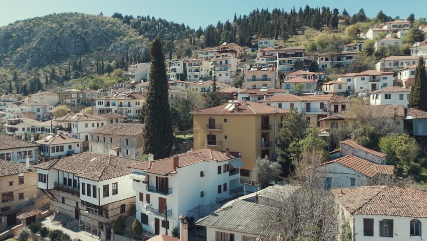 Drone flying upwards, above a village on a green hill in Europe, red roof tops, little houses, sunny weather, Greece 4K video