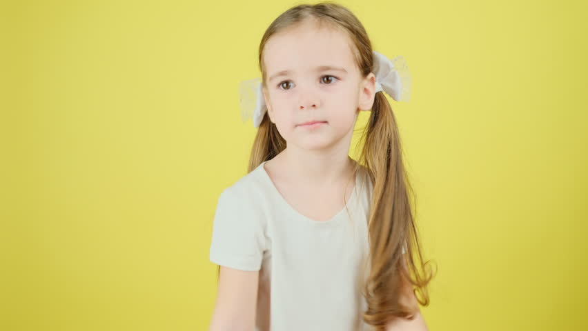 Portrait of a beautiful adorable little girl in a white t-shirt, saying yes, nodding her head at the camera on a yellow background