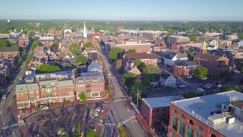 Drone shot pulling back from downtown Portsmouth, NH to reveal the drawbridge over the river. It is early morning with the warm sunrise reflecting on the buildings and bridge.