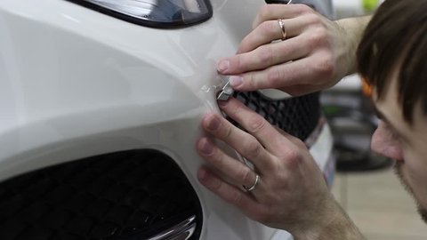 Close up shot of the hands of man who unstick the film with white cowl expensive car. This film protects the vehicle from the rough painting.  car wrap protection film paint