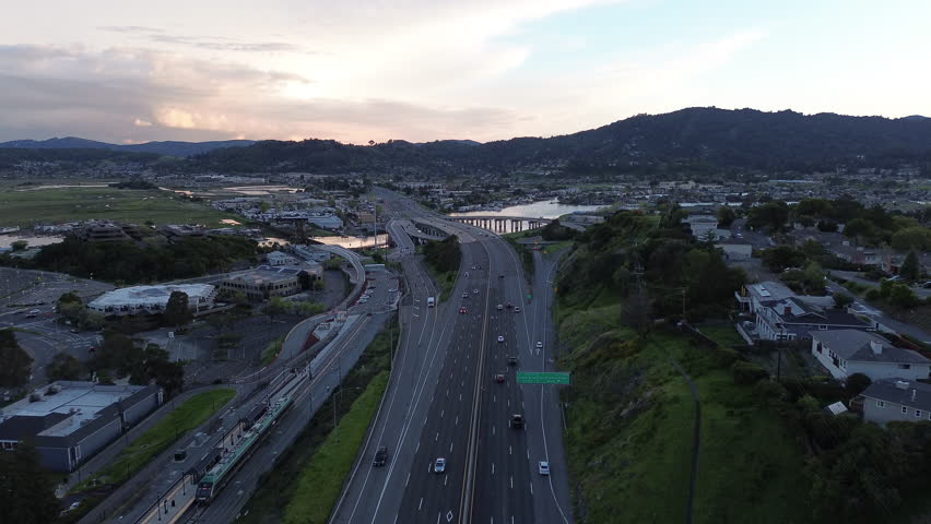 arial of highway through town over river leading into mountains and hills during golden hour sunset	