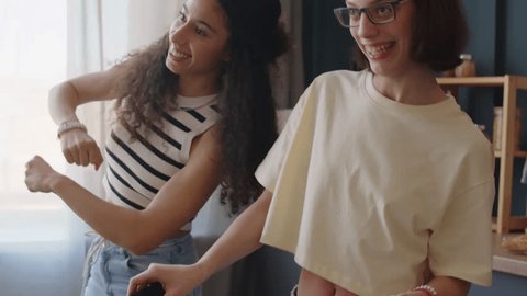 Medium shot of Caucasian teenage girl with cerebral palsy using walking stick while dancing at home with Biracial female best friend having fun together स्टॉक व्हिडिओ