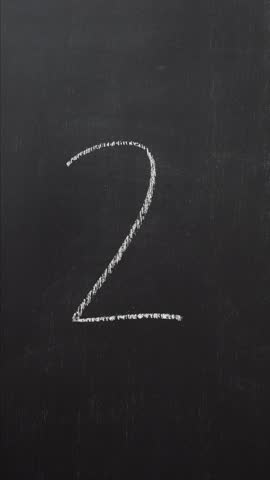 Hand writes the number 2 with white chalk on a black board. Vertical video