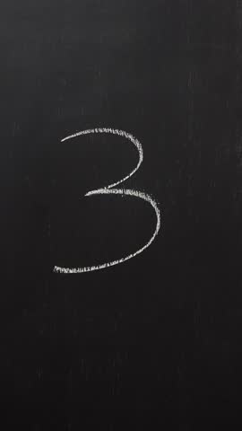 Hand writes the number 3 with white chalk on a black board. Vertical video