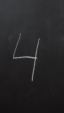 Hand writes the number 4 with white chalk on a black board. Vertical video
