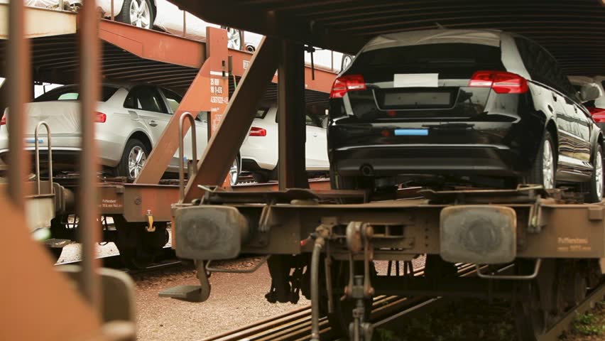 Cars loaded on a train carriage, partially covered, at an industrial depot