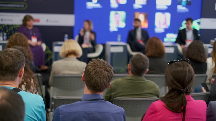 Audience attentively listening at a corporate conference panel discussion. Expert speakers address topics on stage, fostering professional engagement and learning.