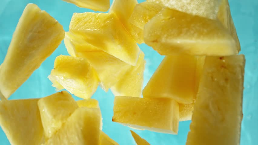 Super Slow Motion of Falling Pineapples Slices into Water, Blue Background. Filmed on High Speed Cinema Camera, 1000 fps. Camera Tracking the Target.