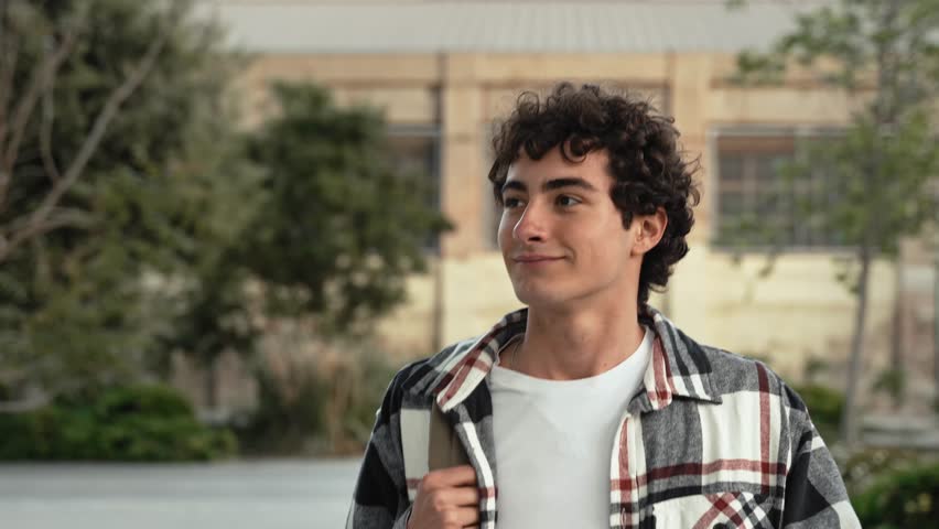 Carefree teenager student walking in the college school campus. Young Inspired man smiling to camera