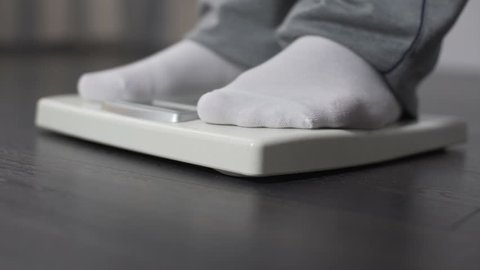 Lazy corpulent male stepping on bathroom scales, weight control and dieting