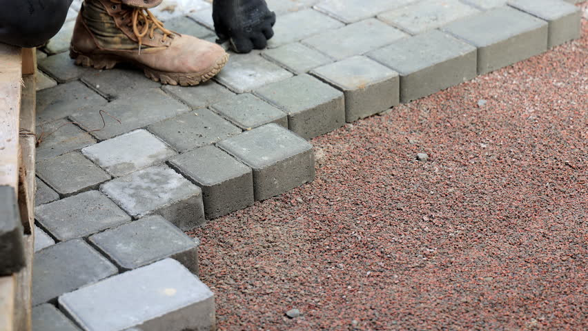 Worker Laying Paving Stones, Close-up of a worker's hands laying gray paving stones on a street, wearing gloves.
