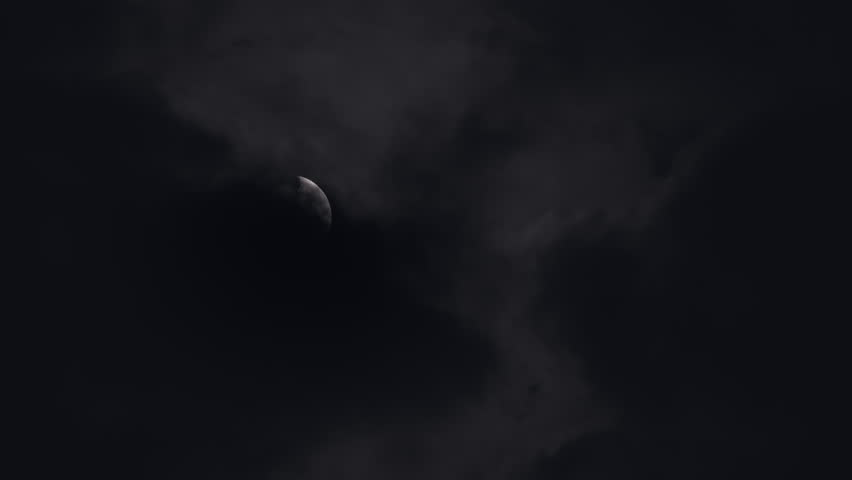 Close up of the Moon in the first quarter surrounded by dark clouds in the night sky