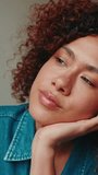 Vertical video, Close-up of dreamy young woman with curly hair wearing denim shirt sitting on sofa in cozy living room