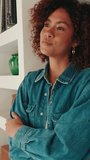 Vertical video, Smiling young woman with curly hair wearing denim shirt looking at camera at home