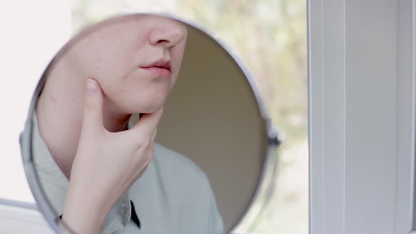 double chin in a caucasian woman. Woman pinching fat on chin and looking at mirror close up