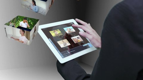 Businesswoman using tablet to view montage of lifestyle clips in holographic form