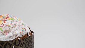 Close-up view of tasty Easter cake (or russian Kulich) with white icing turning against gray background. Real time video. Copy space. Russian words translation: part of phrase 