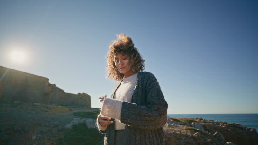 Romantic model resting marine landscape at autumn windy weather zoom on. Elegant attractive woman holding flower looking distance on stones