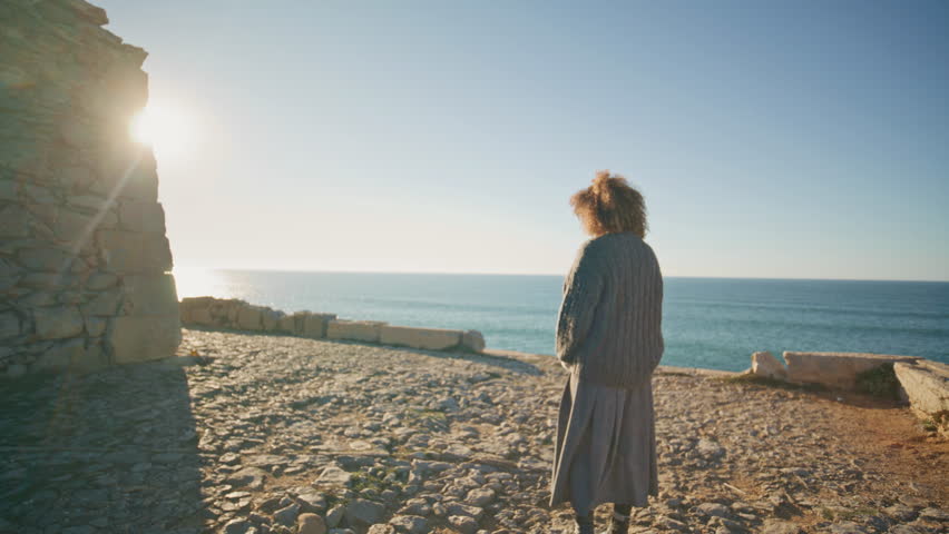 Lonely girl walking marine hill at evening. Serene woman looking rocks standing mountain landscape on sunset. Traveler relaxing ocean view