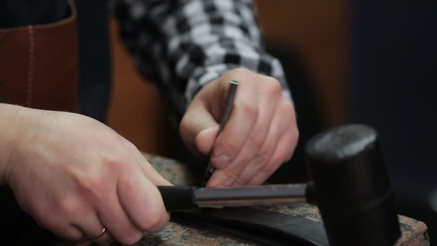 Working process of the leather belt in the leather workshop. Man holding crafting tool and working. He is placing billet to sturdy stand, fixing round knife on a mark and hitting with a small hammer Royalty-Free Stock Footage #35030953