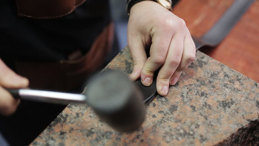 Working process of the leather belt in the leather workshop. Man holding crafting tool and working. He is placing billet to sturdy stand, fixing round knife on a mark and hitting with a small hammer Royalty-Free Stock Footage #35030962