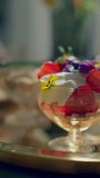 Closeups of overnight oats with berries and edible flowers served in vintage glasses on a golden tray. Healthy breakfast concept. Vertical video. Tilting up
