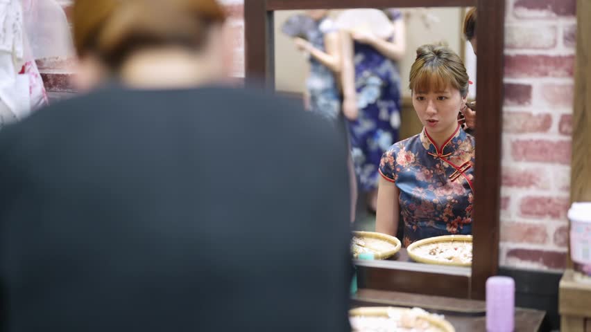 A graceful young Taiwanese woman in a vibrant cheongsam sits for styling in a quaint historic alley in Bopiliao, Wanhua District of Taipei, surrounded by traditional wares and storefronts.