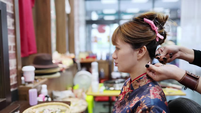 A graceful young Taiwanese woman in a vibrant cheongsam sits for styling in a quaint historic alley in Bopiliao, Wanhua District of Taipei, surrounded by traditional wares and storefronts.