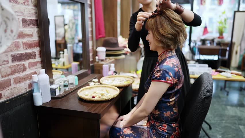 A graceful young Taiwanese woman in a vibrant cheongsam sits for styling in a quaint historic alley in Bopiliao, Wanhua District of Taipei, surrounded by traditional wares and storefronts.