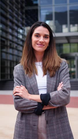 Vertical portrait of cheerful Caucasian business woman with long hair in formal suit looking at the camera with confident expression. Entrepreneur female happy in front building office. Smiling people