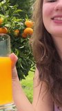 a teenage girl on the background of an orange tree in her hands with a glass of orange juice winks into the frame and makes faces. High quality photo