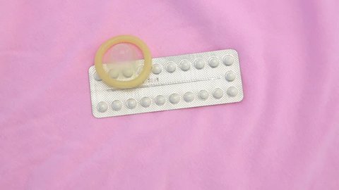 Contraceptive pill packet with condom on revolving pink blanket