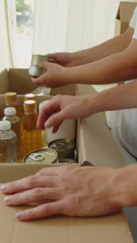 Vertical shot of hands of donation center volunteers giving food to people in need