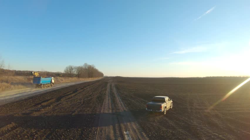 Off road vehicle riding along ploughed meadow. Pickup truck driving through plowed field at sunset time. Black car going on route with sunlight at background. Concept of agronomy farming. Aerial shot