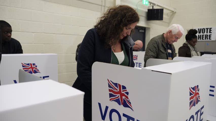4K: Caucasian Female Voter voting at Polling Place for the UK Election.  50-54 years. People vote at booths. Gimbal up. Stock Video Clip Footage