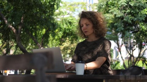 Young Woman Using Laptop Outdoors In Park With Coffee. 4K.