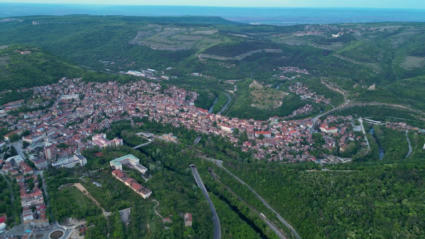 Aerial drone shot of the city of Veliko Tarnovo in Bulgaria. Yantra river,  Tsarevets, Trapezitsa, and Sveta Gora seen from above. High angle footage of residential and industrial buildings at dusk.