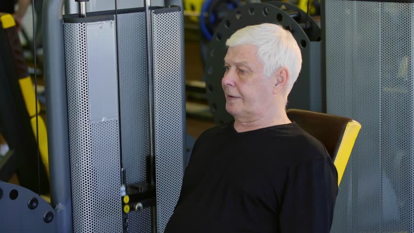 An elderly man is working out in the gym