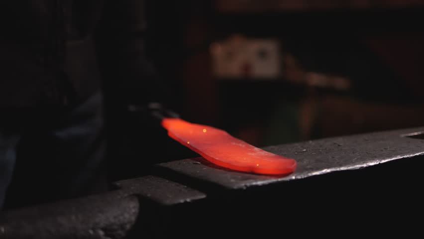 Craftsman workshop.  man master in blacksmith shop beats hot iron on an anvil with hand hammer. blacksmith works in workshop. process of creating  metal product in forge. Close-up