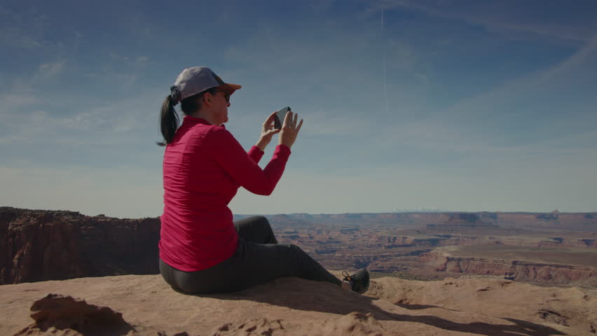 Woman sitting on overlook photographing scenic view at canyonlands national park, utah, united states