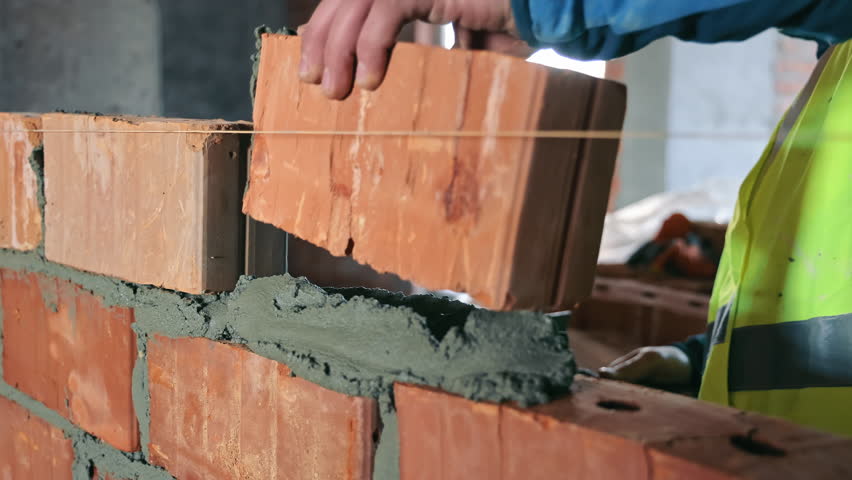 Close-up of Mortar Application on Brick Wall, Close-up of a construction worker's hands applying mortar on a brick wall, demonstrating precision in bricklaying techniques.