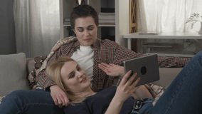 Lesbian couple is resting on the couch, and having video conversation with friend, waving their arms, video call 60 fps