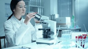 Professional female scientist looking through microscope and taking notes during research at workplace in medical laboratory - Powered by Shutterstock - Get 15% off with code: PIKWIZARD15