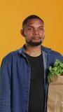 Vertical Video African american secretive guy doing mute hush gesture with finger over lips, keeping a secret about locally grown organic produce in a paper bag. Person being private about veganism